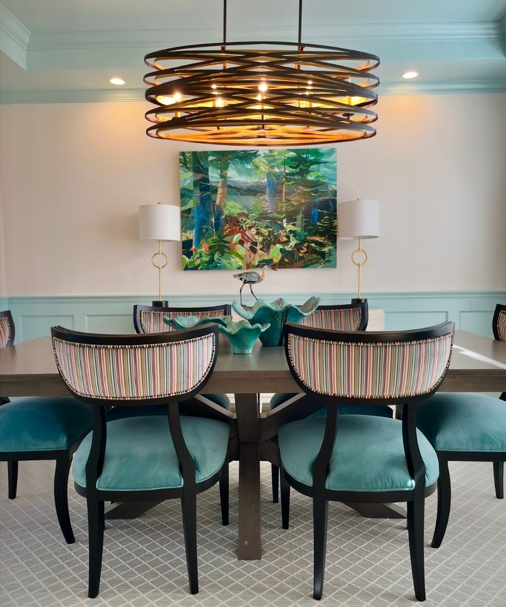 Dining room with a rectangular table and striped upholstered chairs, featuring a decorative chandelier and wall art.