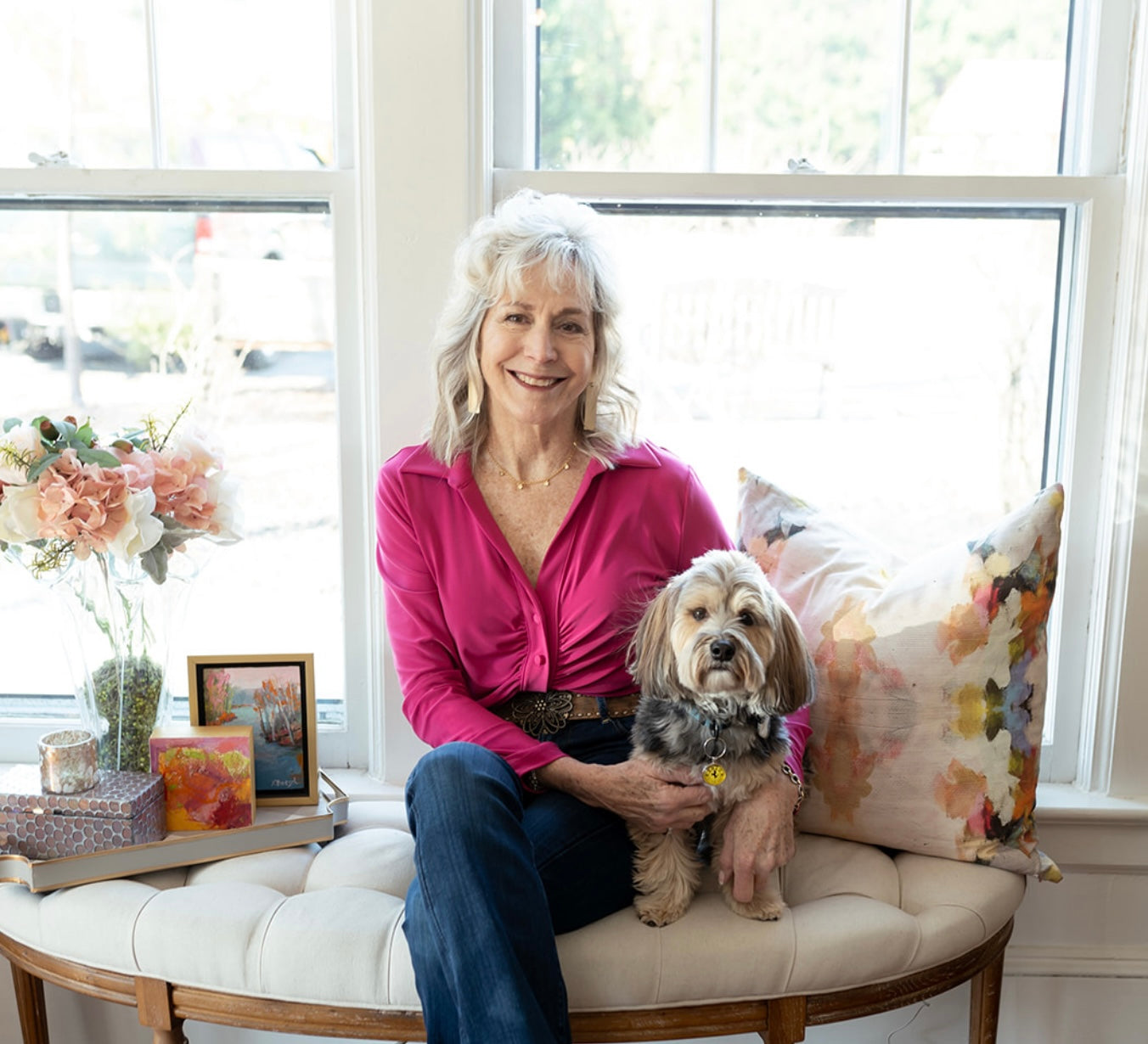 Photo of Lori Savio, Interior Designer, seated by a window at Home, Heart & Soul design center boutique with her arms around her dog