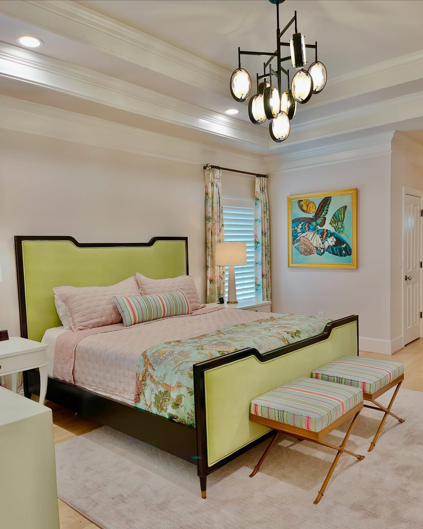 Photo of a bedroom after an interior design transformation. Butterfly artwork on the wall with modern lighting, a bed with light green headboard and light pink bedding.