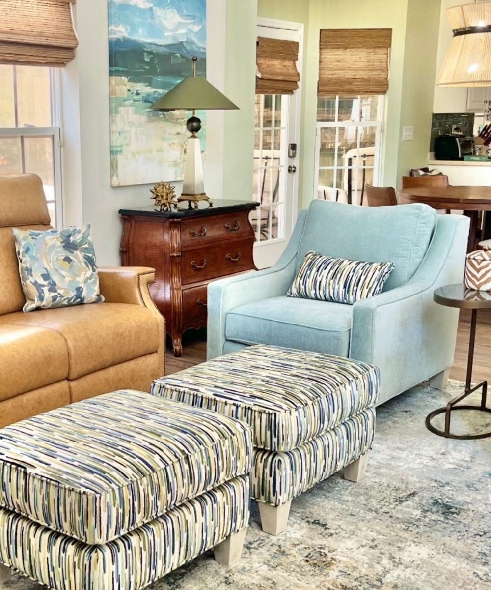 Living room with a brown sofa, blue armchair, and striped ottomans.
