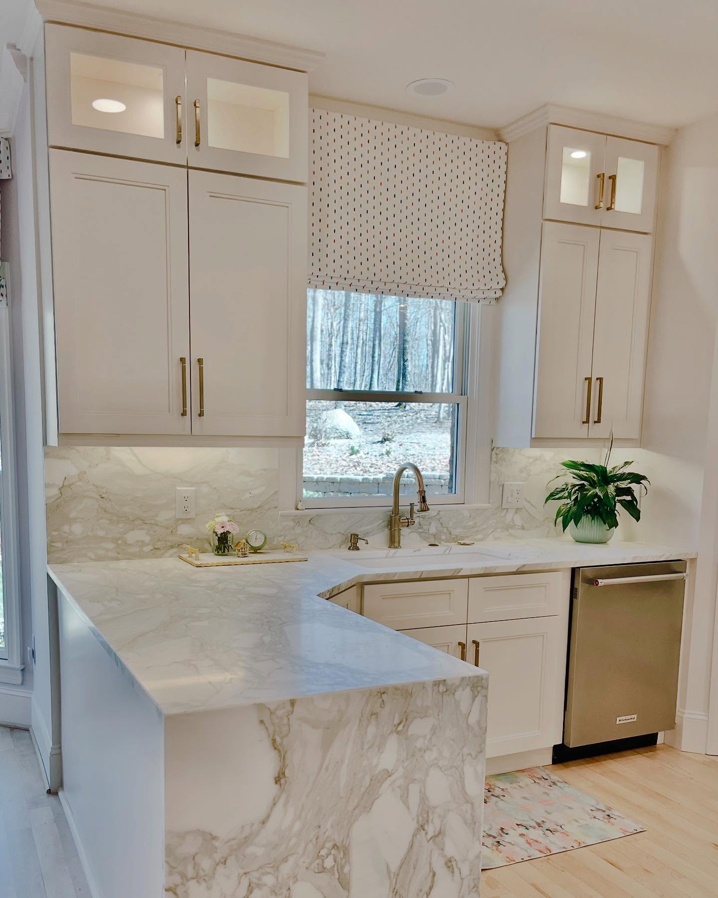Photo of a newly remodeled kitchen in Davidson with a beautiful waterfall countertop, full backsplash in Calcutta gold marble, and custom cabinetry to the ceiling painted in Sherwin-Williams Marshmallow.
