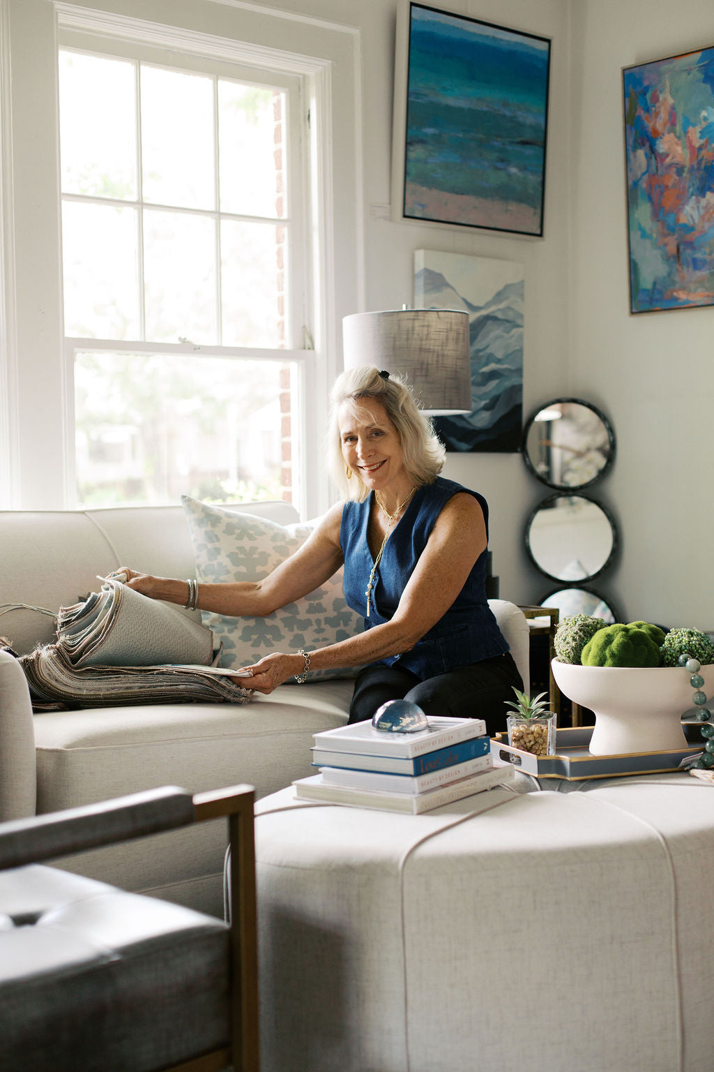 Lori Savio is sitting on a couch in the stylish living room of her boutique design center with fabric samples.