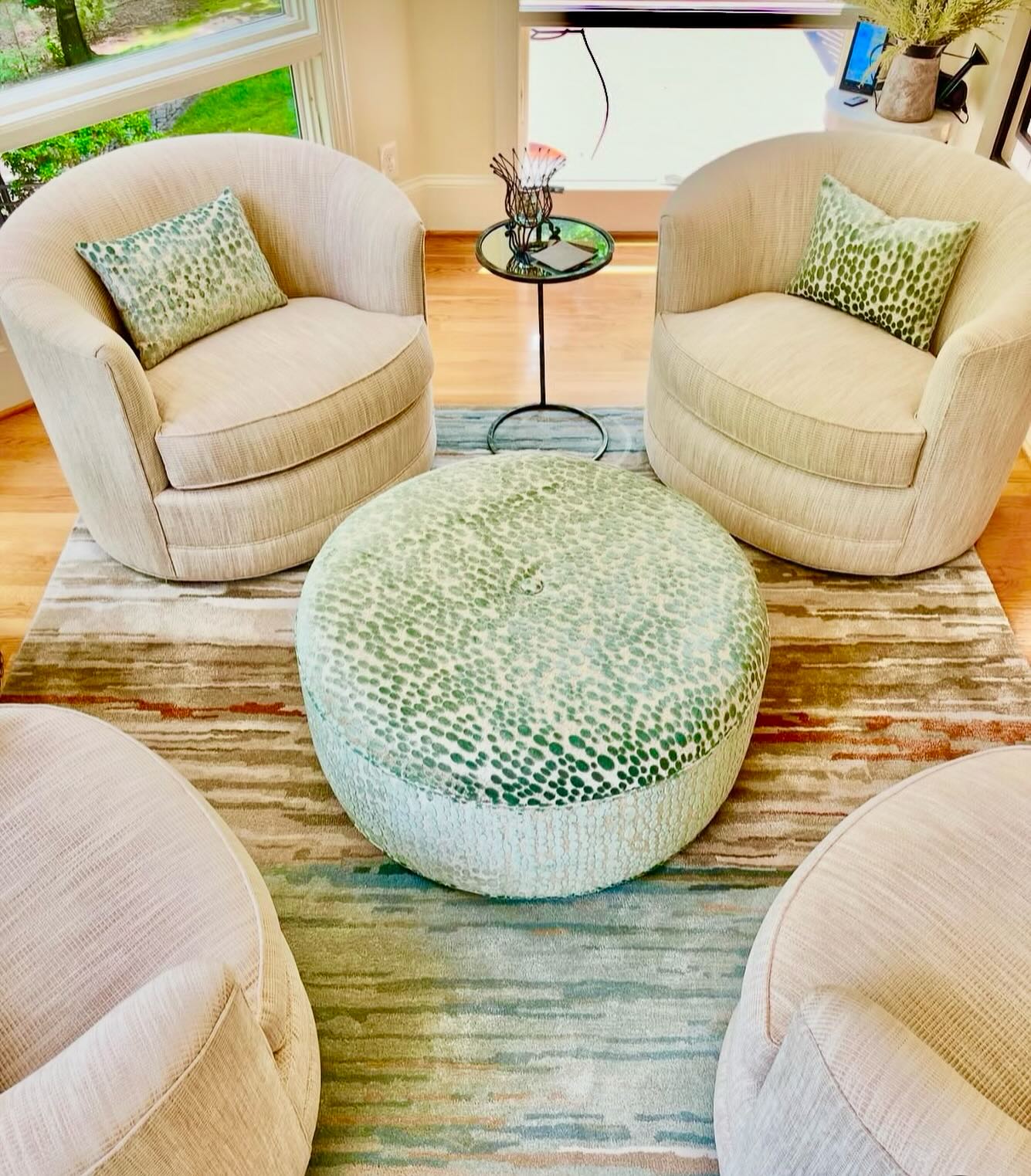 Photo of a beautiful sitting or conversation area with plush circular chairs, rich green pillows, and a beautiful multicolored rug that matches.